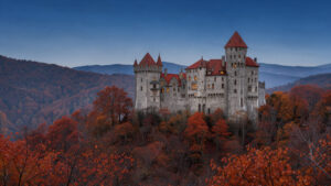 Le château de Bran se détache au crépuscule au-dessus d’une forêt rousse des Carpates, sous un ciel bleu sombre.